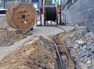 Wooden coil of electric cable and optical fibres in the digging on the street construction site