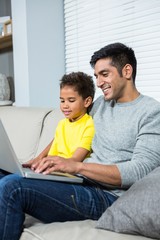Smiling father and son using laptop on the sofa