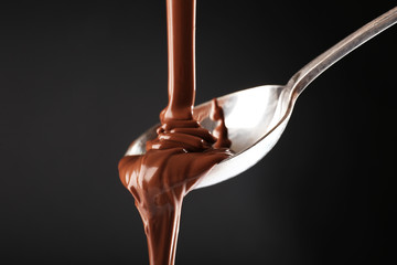 Chocolate poured on a spoon on dark background