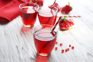 Three glasses of tasty juice and garnet fruit, on wooden background