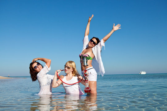 Three beautiful girls smoke shisha at the seaside on holiday