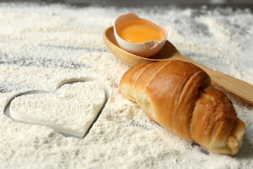 Heart of flour, croissant and wooden spoon on gray background