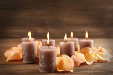 Fototapeta na wymiar Alight wax grey candle with flower petals on wooden background
