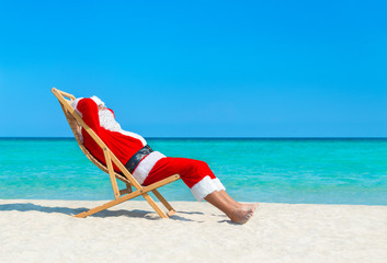 Christmas Santa Claus resting on sunlounger at ocean sandy tropical beach