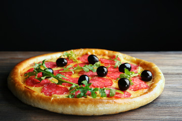 Tasty pizza with salami and olives on wooden table against black background