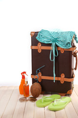 Valise with summer items on wooden board on white background