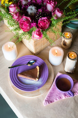 Obraz na płótnie Canvas Piece of delicious chocolate mousse cake on colorful plate on wooden table background. Table setting with flowers and candles for tea party. Selective focus.