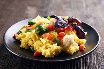 Rice with vegetables on black plate on wooden background