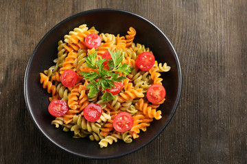 Delicious macaroni dish in black bowl on wooden background