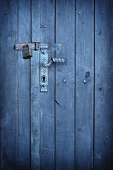 Old vintage door handle with a rusty padlock on a stunning blue colored wood door