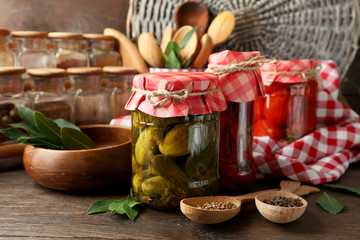 Jars with pickled vegetables and beans, spices, book of recipes and kitchen utensils on wooden background