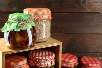 Jars with pickled vegetables and beans on wooden background