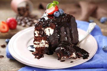 Chocolate cake with cream and fresh berries on plate, on wooden background