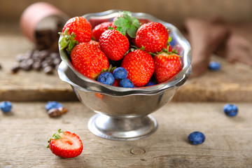 Ripe sweet different berries in bowl, on old wooden table