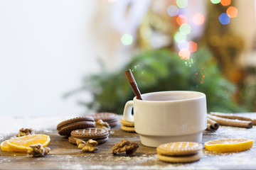 Tea with lemon, tangerines, cookies and nuts in Christmas decor with Christmas tree, nuts and apples on colorful background bokeh