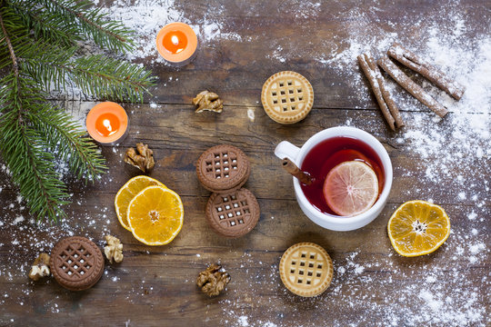 Tea, tangerines and cookies in Christmas decor with Christmas tree, nuts and apples on dark wooden background