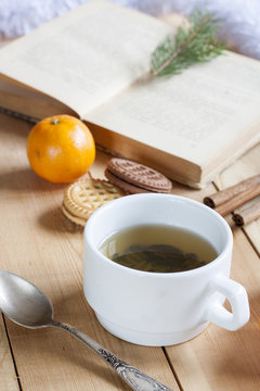 Cup of hot tea with books, cookies and tangerines on light wooden table.