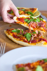 Female hand grabs for a slice of italian style pizza with arugula and prosciutto
