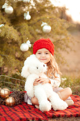 Smiling kid girl holding white teddy bear with christmas decorations outdoors. Childhood. Looking at camera. 