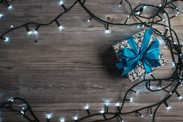 Christmas gift box with blue bow and lights on wooden surface