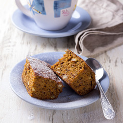Homemade carrot and banana cake with nuts and spices, sprinkled with powdered sugar and a cup of tea on white vintage surface