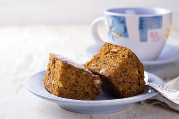 Homemade carrot and banana cake with nuts and spices, sprinkled with powdered sugar and a cup of tea on white vintage surface