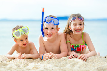 Young playful children with scuba gear lying on the sand at the beach