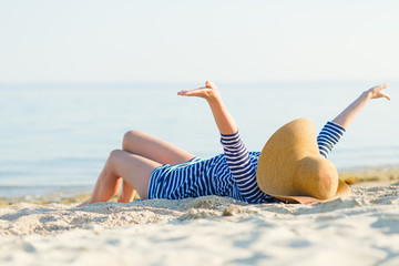 Woman with a straw hat lying on the sand with arms spread open at the beach