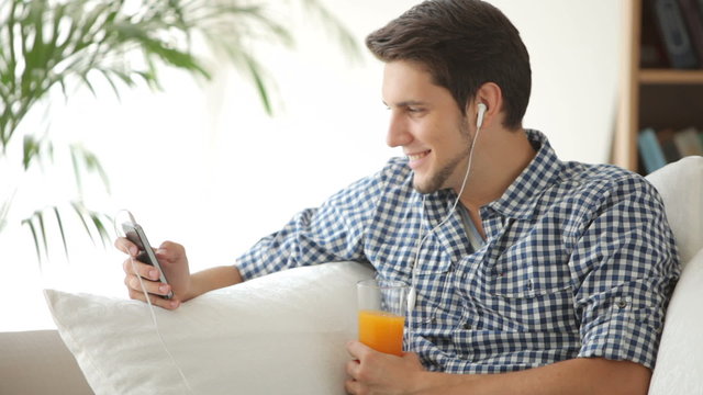 Handsome guy sitting on couch and listening to music with earphones