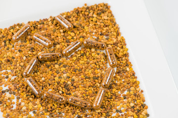 Heart of homeopathic pills with bee pollen on a white plate (sha
