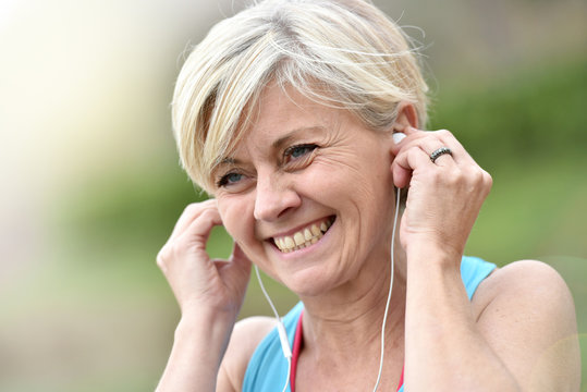 Portrait of senior woman adjusting earphones before exercising - Powered by Adobe