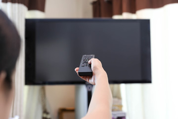 Hand holding TV remote control changing television channel