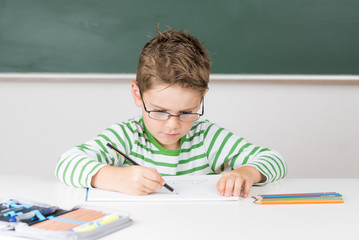 Kleines Kind mit Brille malt aufmerksam an einem Bild