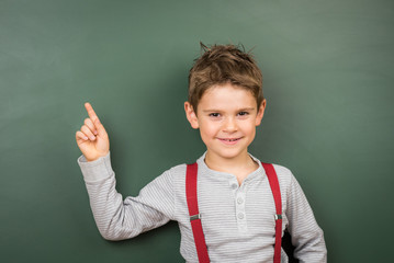 Hübscher kleiner Junge deutet auf leere Schultafel