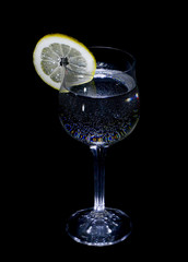 A glass of water and lemon in the dark.