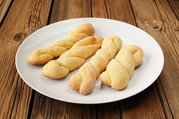 Twisted cookies on white plate on old wooden table