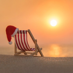 Deckchair with christmas santa hat at ocean beach during sunset