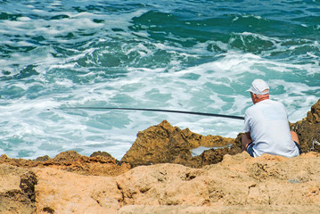 Man fishing on rocks by the sea.