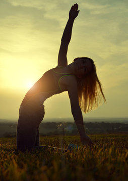 Silhouette of young woman stretching on a meadow at sunset