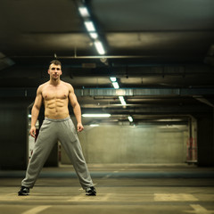 Fototapeta na wymiar Handsome muscular young man stretching at parking garage, natural lights, dark place.