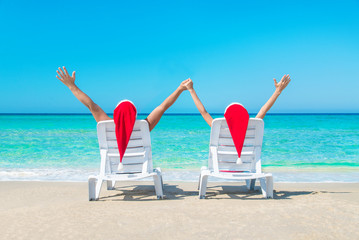 Obraz premium Young couple hands up in sunloungers at ocean beach