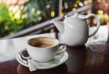 Cup of coffee with hot tea pot on wooden and blur background