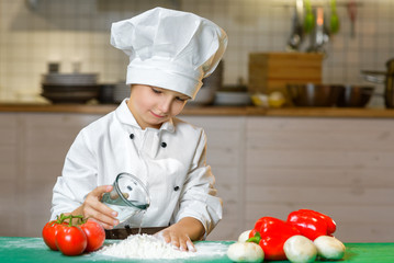 Funny happy chef boy cooking at restaurant kitchen and pours water into the dough - 96623886