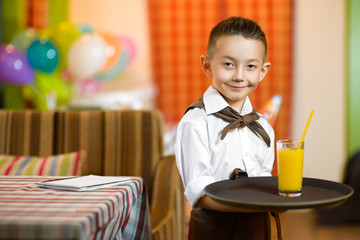 Happy cute little boy smiling waiter holding a tray width juice