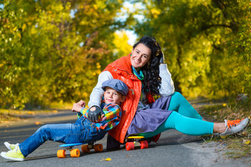 Fototapeta na wymiar Smiling woman and boy sitting on color plastic penny boards or skateboards outdoor