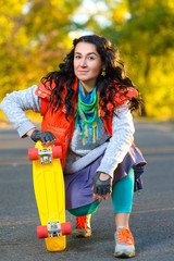Fototapeta premium Smiling woman sitting near color plastic penny board or skateboard outdoor