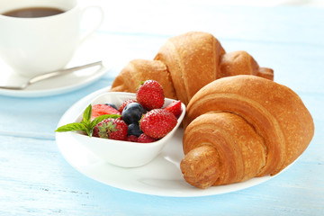 Fresh tasty croissants with berries on blue wooden background
