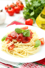 Spaghetti with tomatoes and basil on plate on white wooden backg