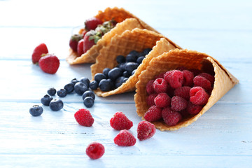 Waffle cones with berries on wooden table