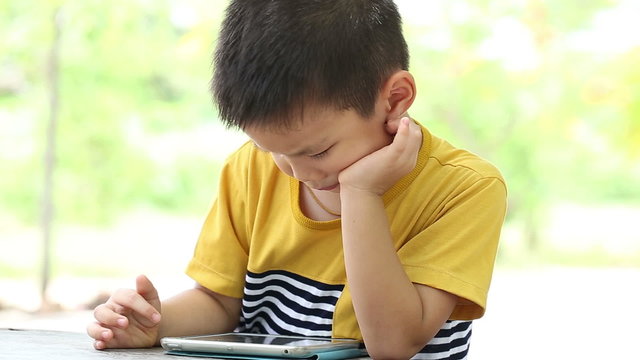 Little handsome boy touch on ipad tablet and playing game on wooden table in park